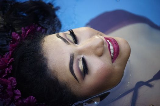 Close-up of a woman with stunning makeup and red lips enjoying a serene moment in water.