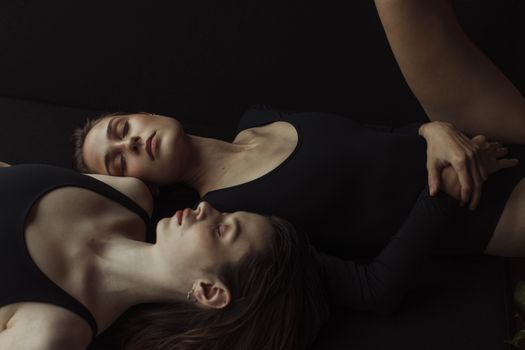 两名女子身穿黑色紧身衣，闭着眼睛躺在地上，营造出一幅宁静而艺术的构图