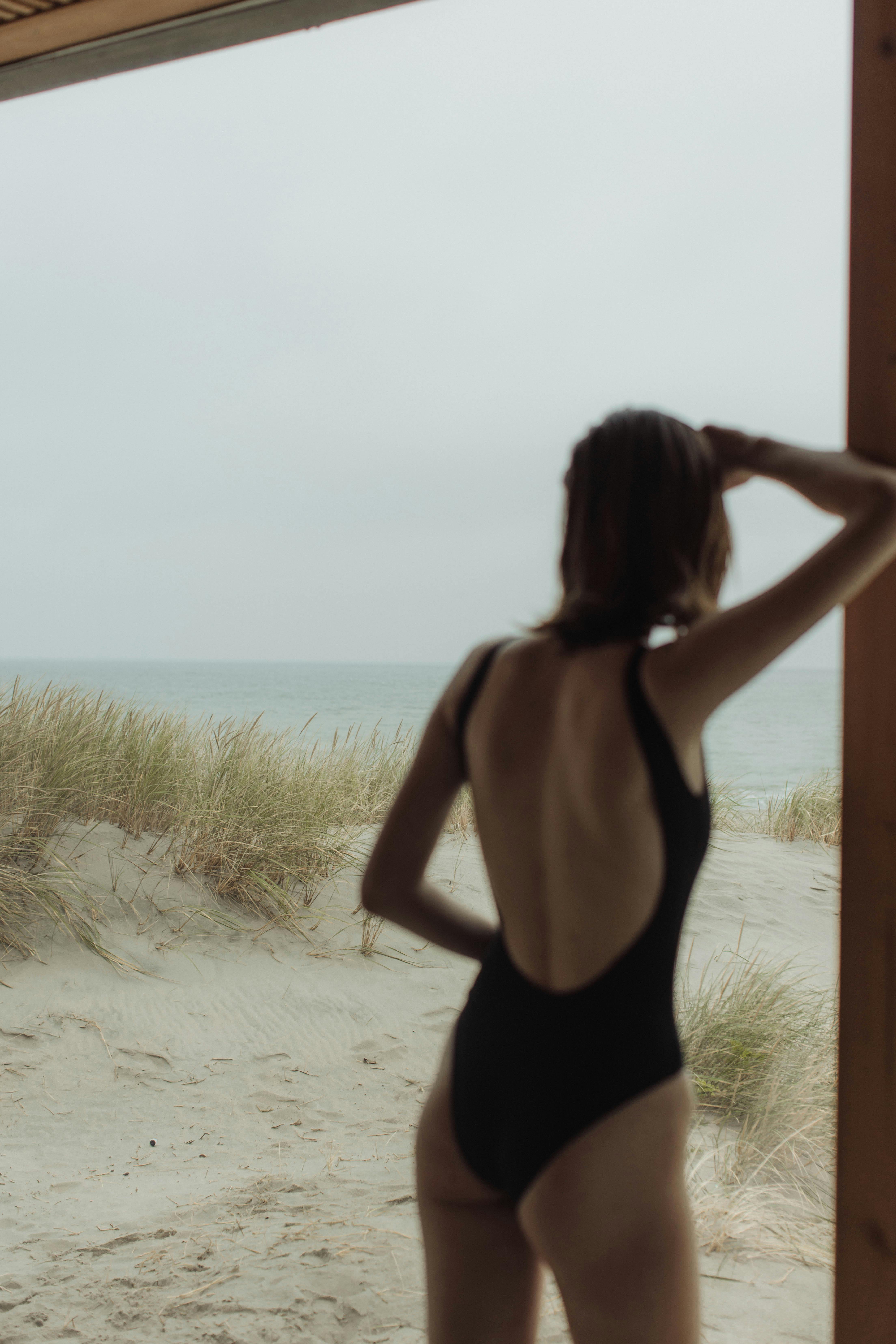 一个穿着黑色泳衣的女人从海滩小屋凝视着大海，体现了宁静的夏日氛围
