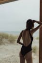 一个穿着黑色泳衣的女人从海滩小屋凝视着大海，体现了宁静的夏日氛围