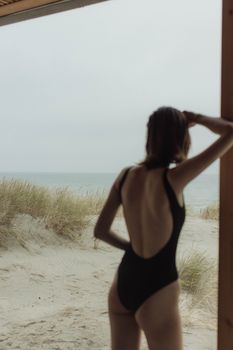 一名身穿黑色泳衣的女子在海滩小屋里凝视着大海，宁静的夏日氛围油然而生