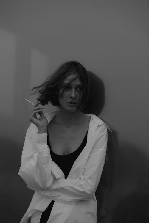 Grayscale Photo of Woman in White Long Sleeve Shirt Smoking a Cigarette