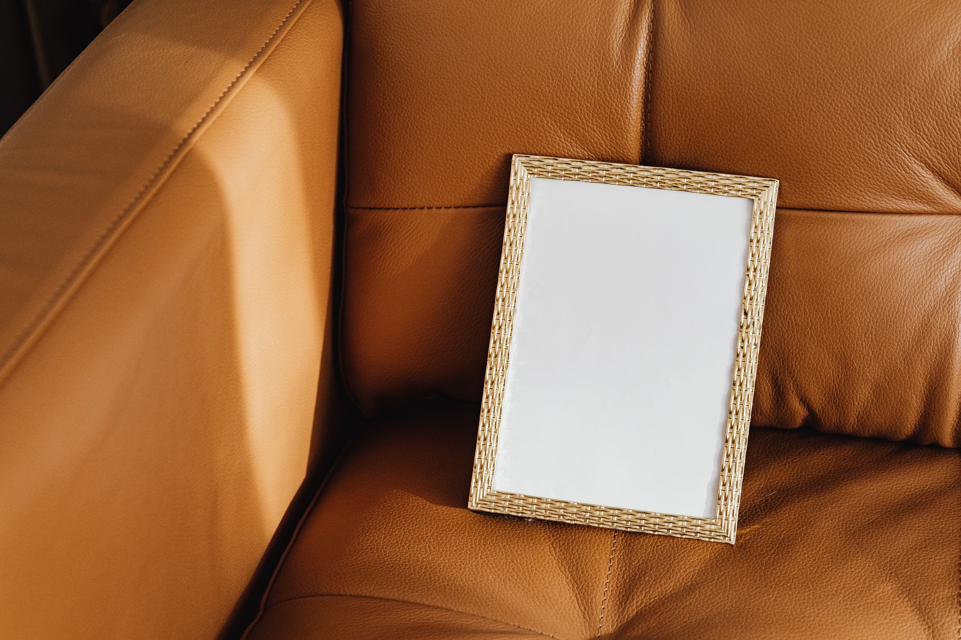 A blank picture frame rests on a brown leather sofa, perfect for mockups.