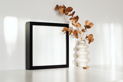 Free A minimalist interior setup featuring a ceramic vase with eucalyptus and a blank picture frame. Stock Photo