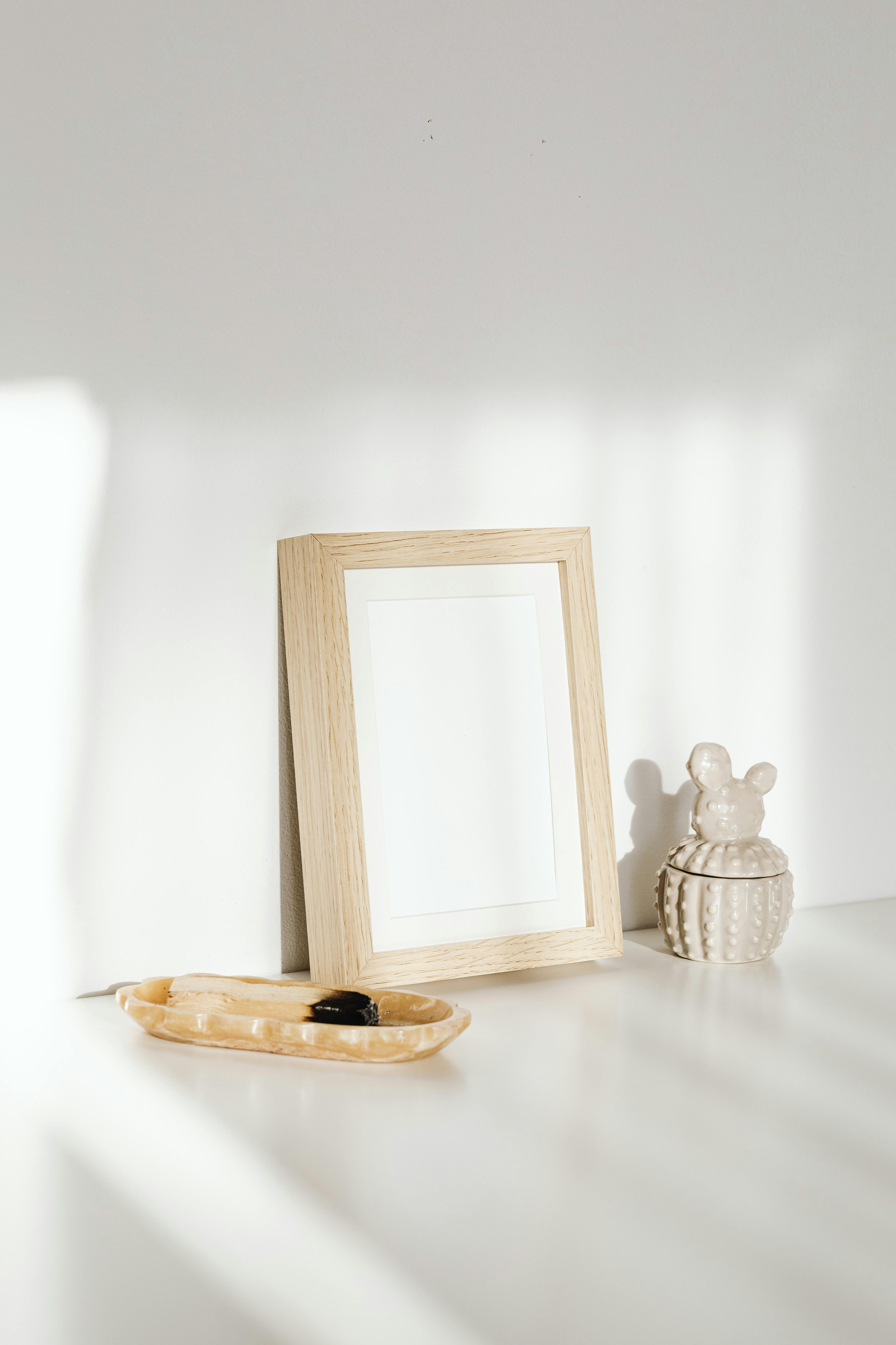 A wooden photo frame placed on a white tabletop with soft sunlight and shadows.