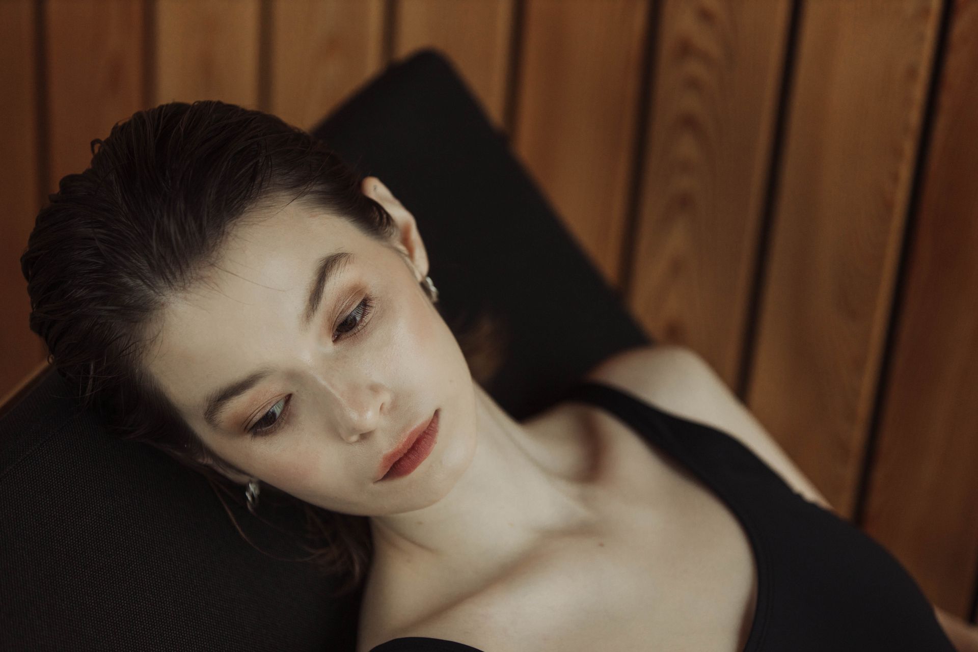 Elegant portrait of a woman in a black tank top with wooden background indoors.