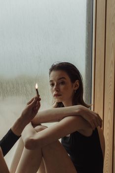 一位体贴的女人坐在窗前，手里拿着一根点燃的火柴，唤起一种平静而内省的情绪
