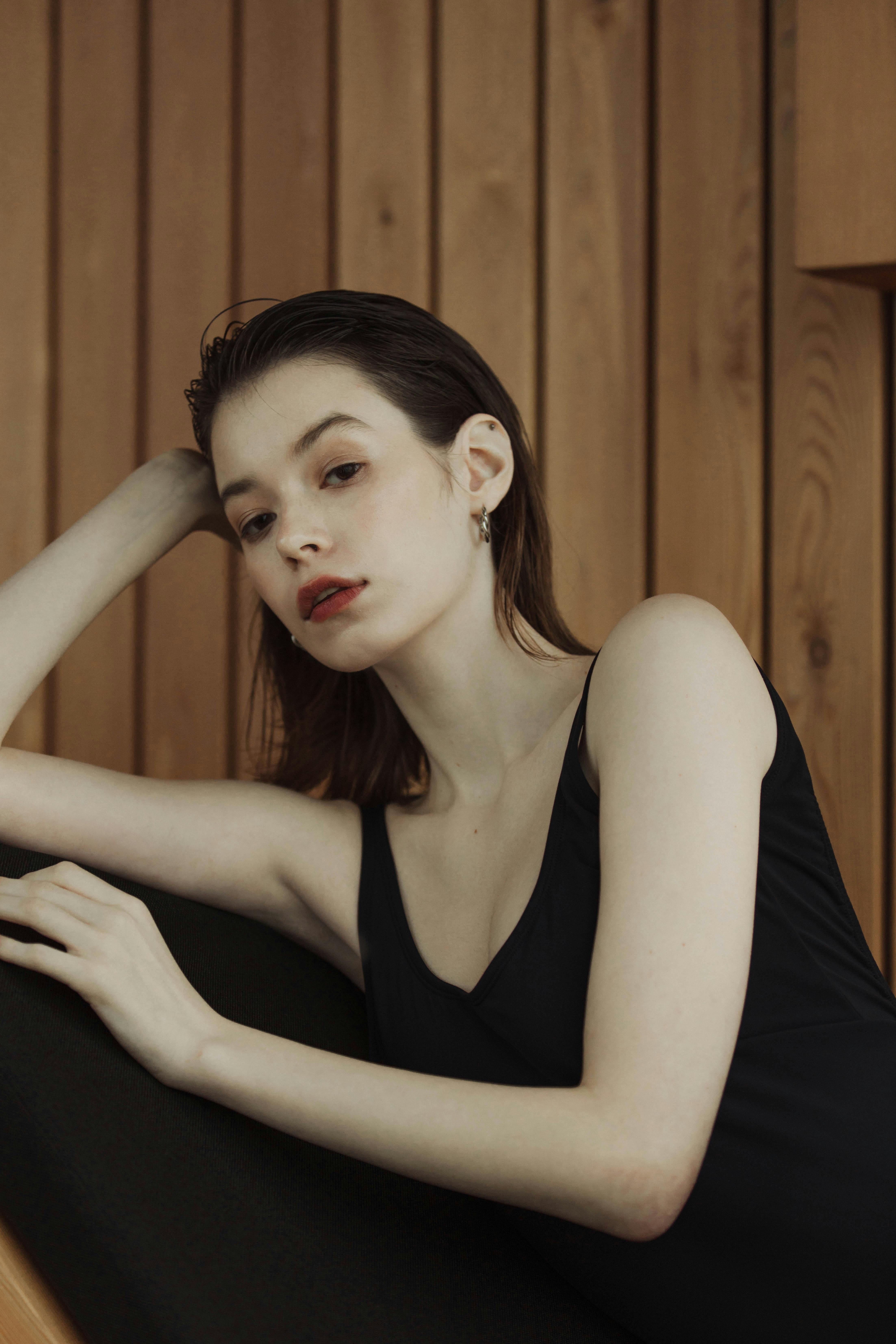 Stylish woman in a black top posing gracefully against a wooden wall, showcasing modern elegance.