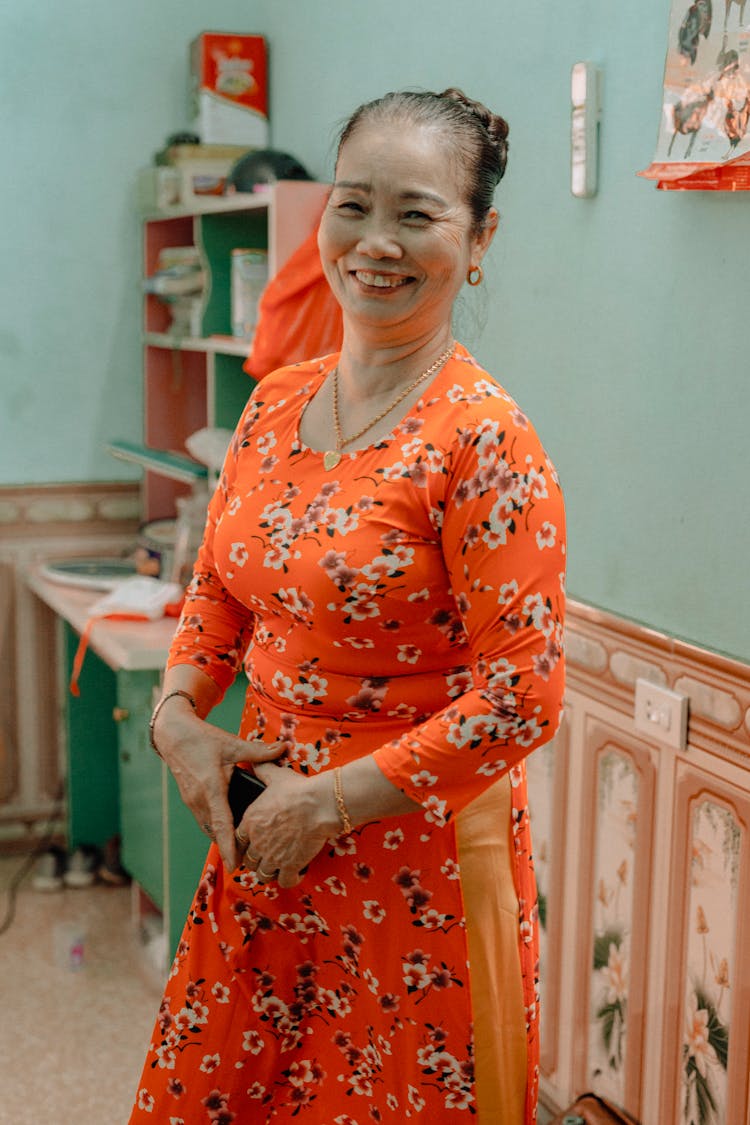 Portrait Of A Cheerful Woman In Orange Dress With Floral Pattern Against Teal Wall