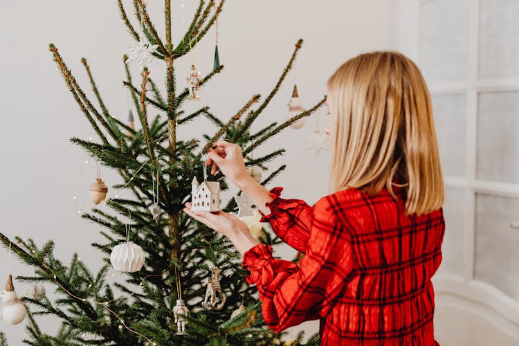 Person Hanging Christmas Ornaments On A Christmas Tree 