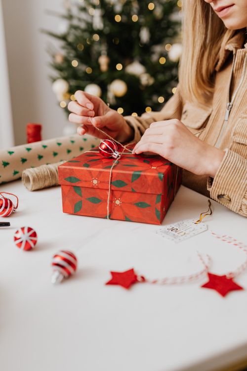 Free A woman wraps a festive Christmas gift with decorations on a table indoors. Stock Photo