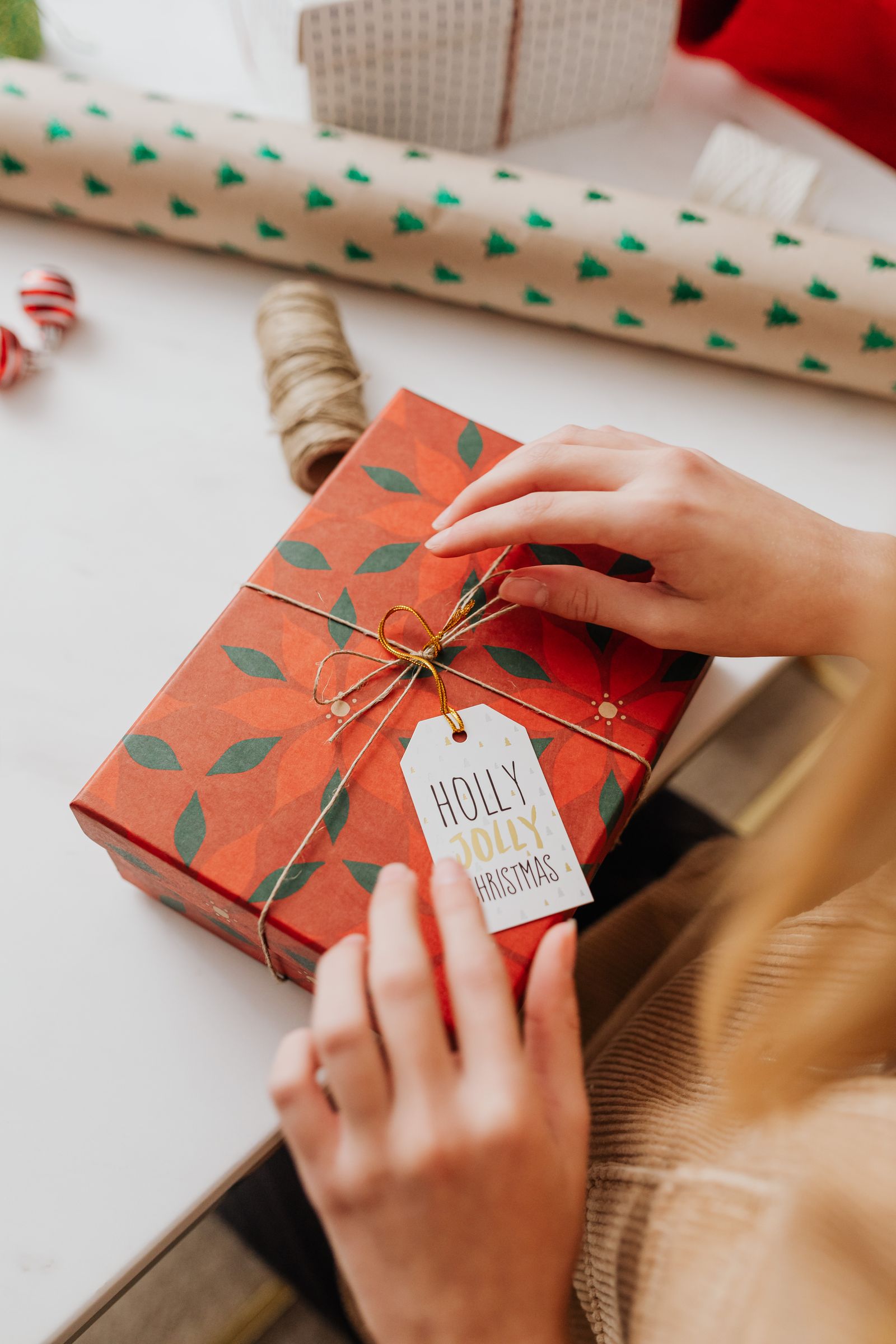 Hands wrapping a Christmas gift in red paper with a holiday gift tag.
