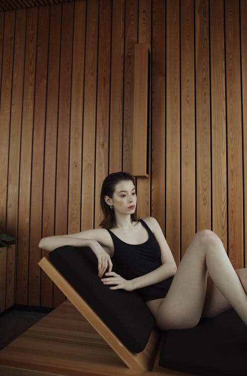A Woman in Black Swimsuit Sitting on the Woode Bench with Black Cushions