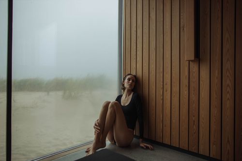 Free A serene moment of a woman sitting by a modern wooden interior with a sandy view. Stock Photo