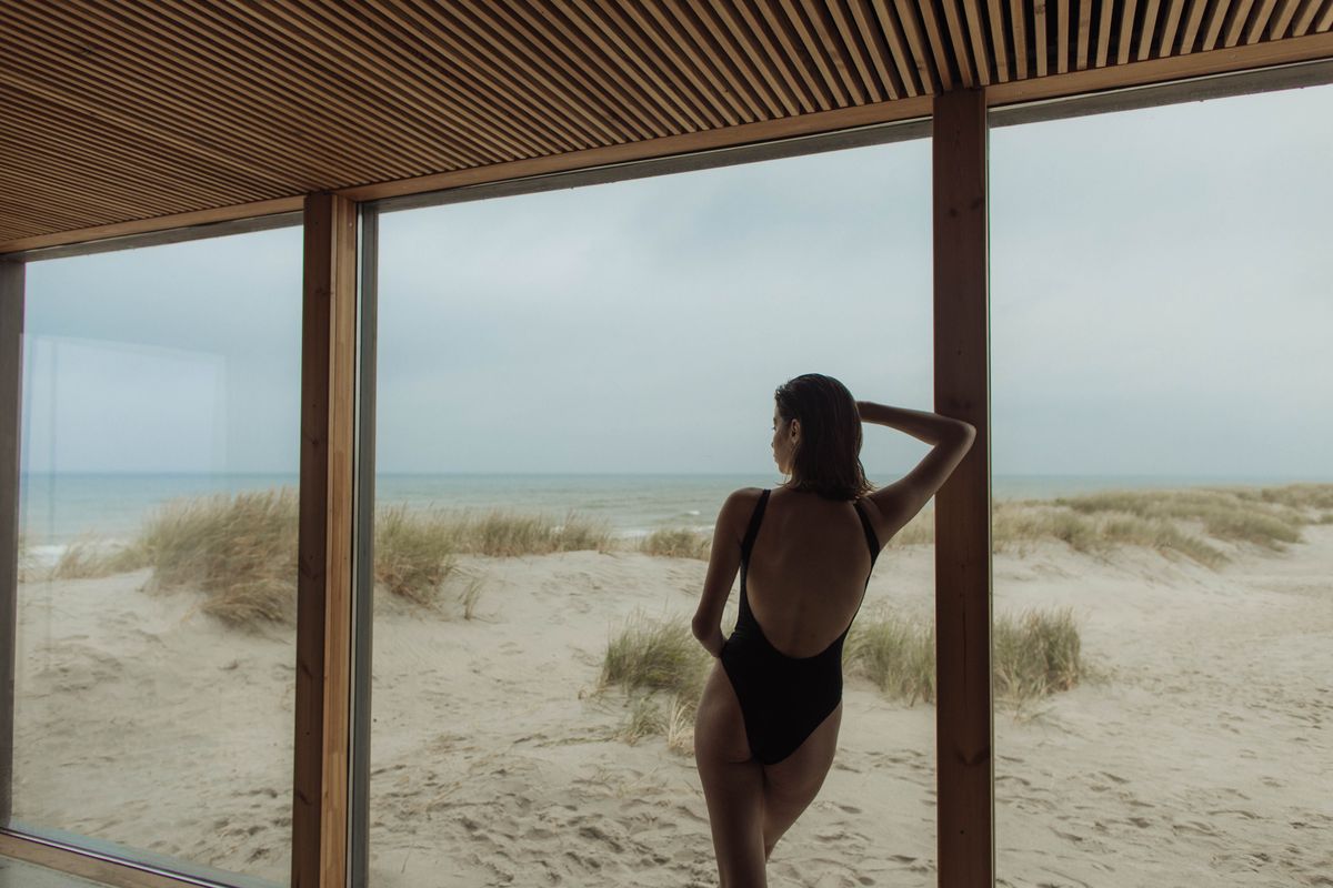 A woman in a black one-piece swimsuit, back view — the sculptural maillot