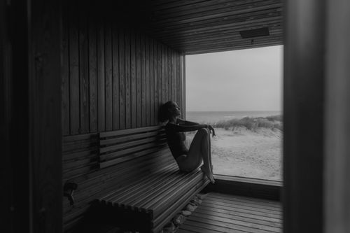 Free Black and white image of a woman sitting in a beachfront sauna, gazing at the sea. Stock Photo