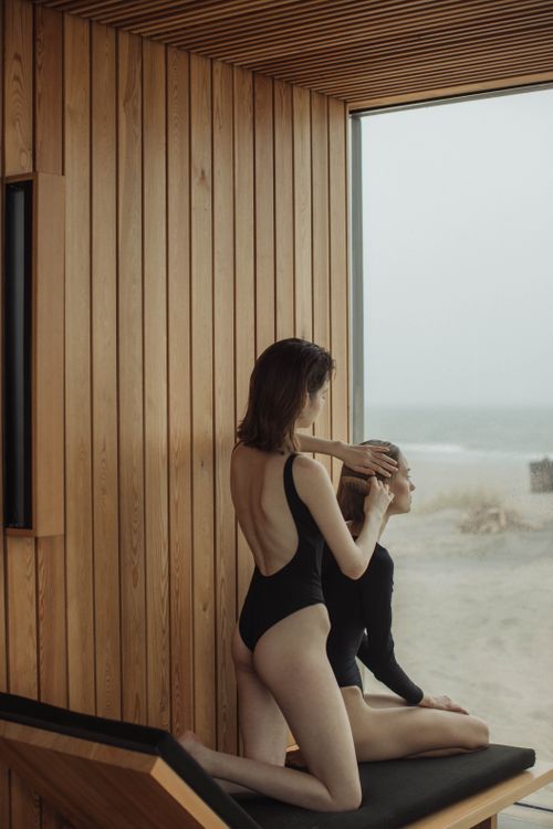 Free Two women in swimsuits enjoying a serene moment with ocean views through a wooden glass wall. Stock Photo