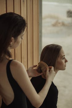A serene moment of a woman combing another woman's hair by a window, reflecting tranquility.