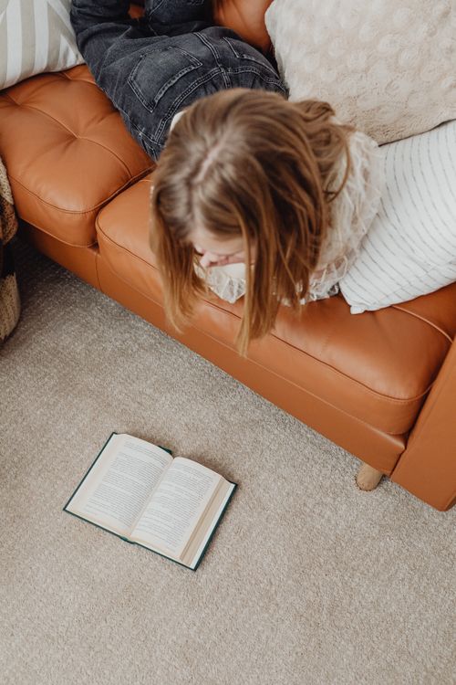 Free Woman lying on a sofa, enjoying a book from a high angle view indoors. Stock Photo