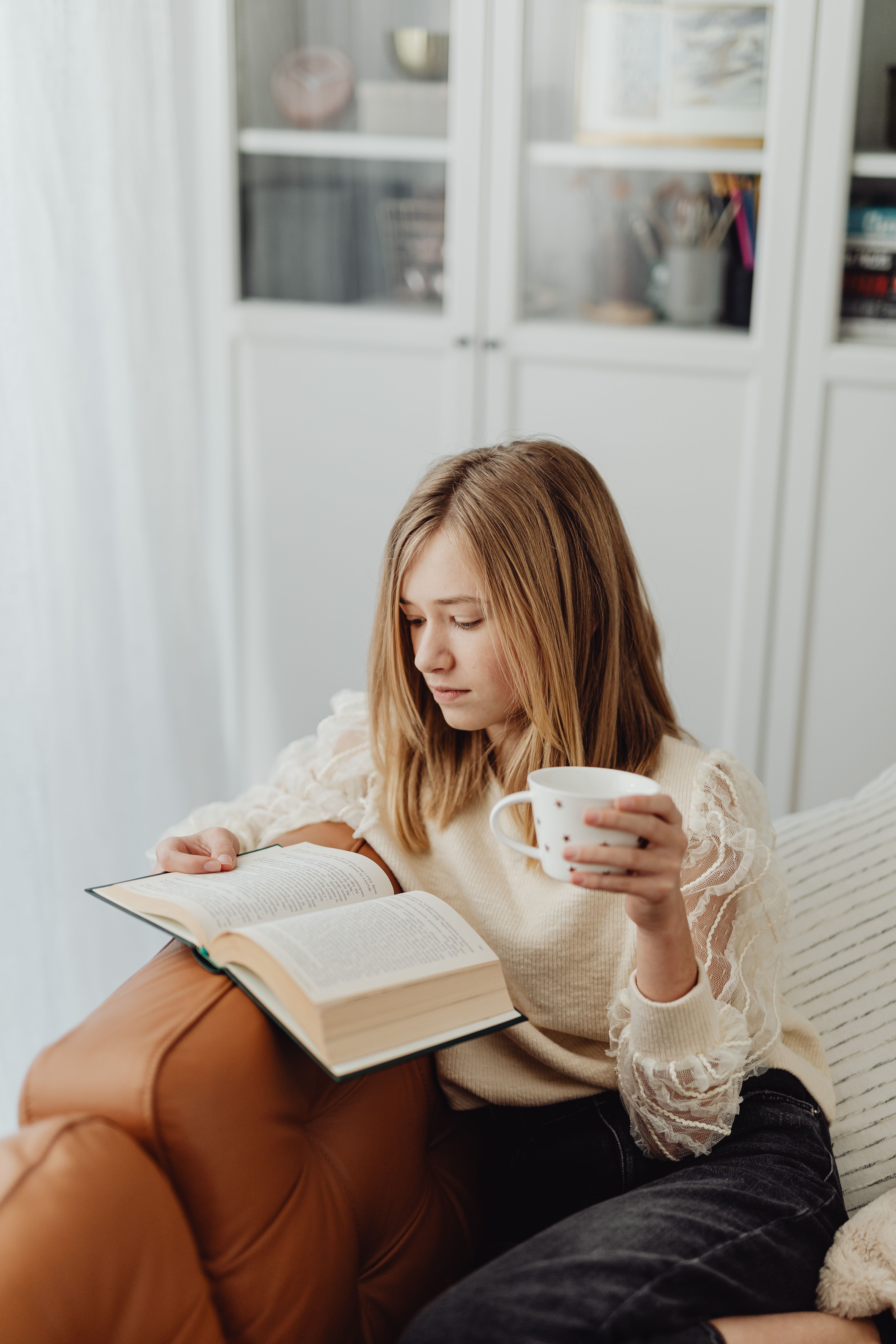 Woman enjoying reading a book on a sofa with a coffee cup indoors.