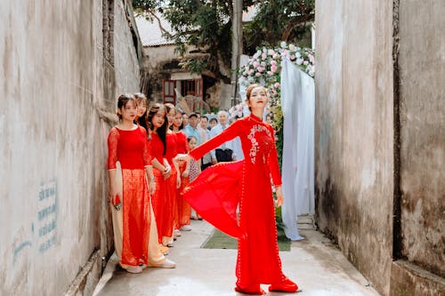 Free Women in Red Long Sleeve Dress Standing on a Narrow Street  Stock Photo
