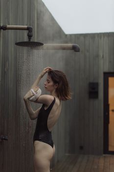 一名女子身穿黑色泳衣，在现代建筑背景下享受户外淋浴