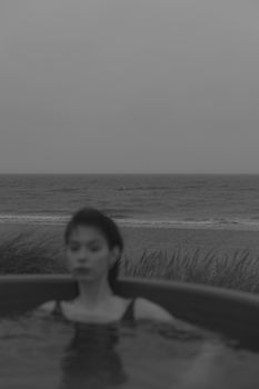 这是一张宁静的黑白照片，照片中一名女子正在海滩边的极可意浴缸里放松