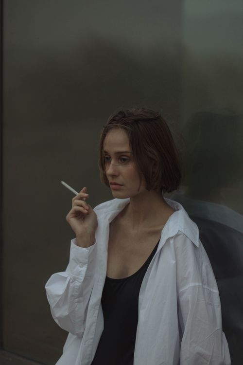 Free Woman in a white shirt holding a cigarette with a contemplative expression. Stock Photo