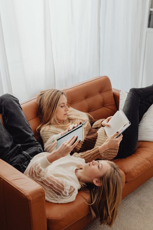 Woman and a Girl Lying Down on Sofa in Opposite Directions and Reading Books