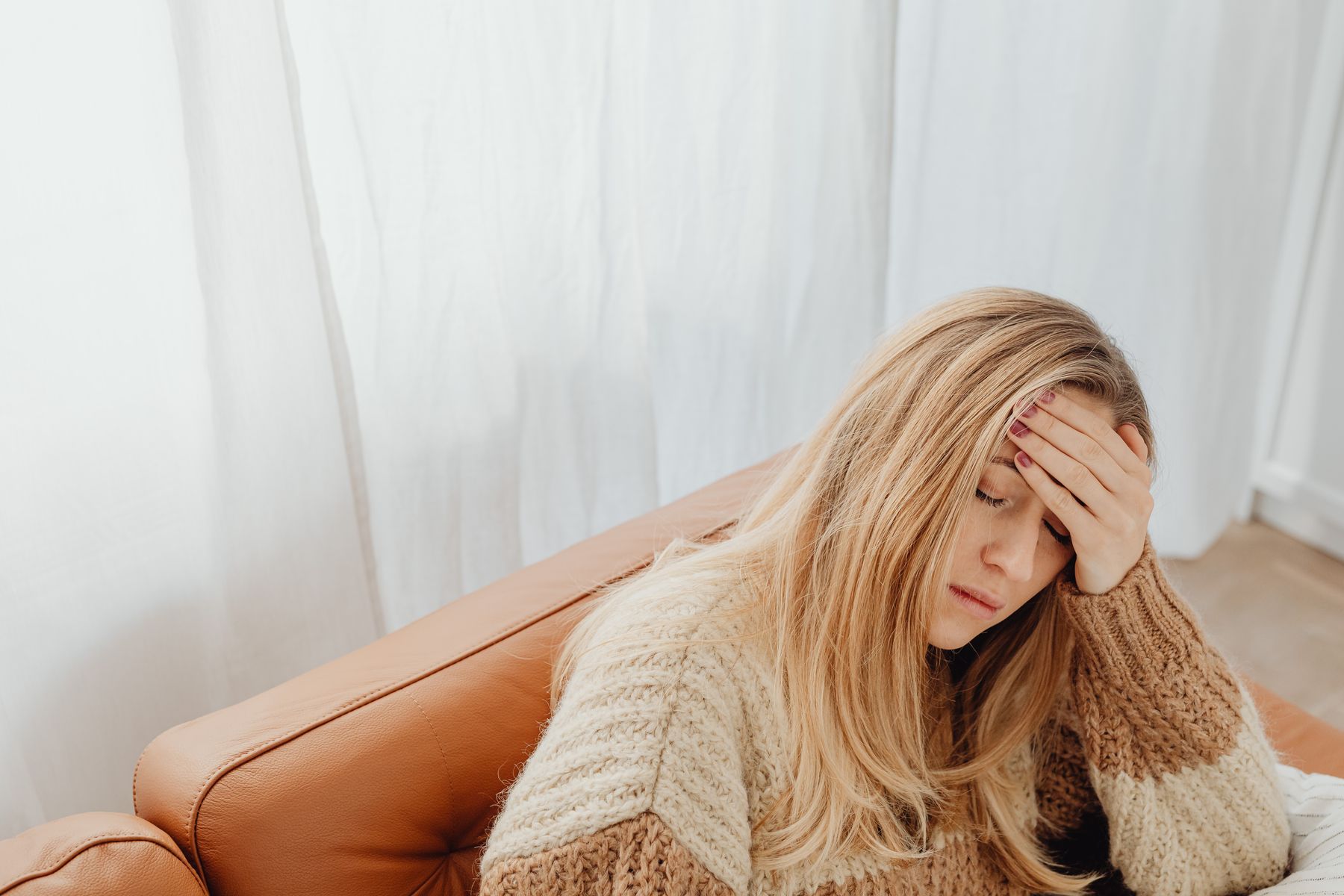 White woman sitting on a couch with her hand on her forehead during a headache