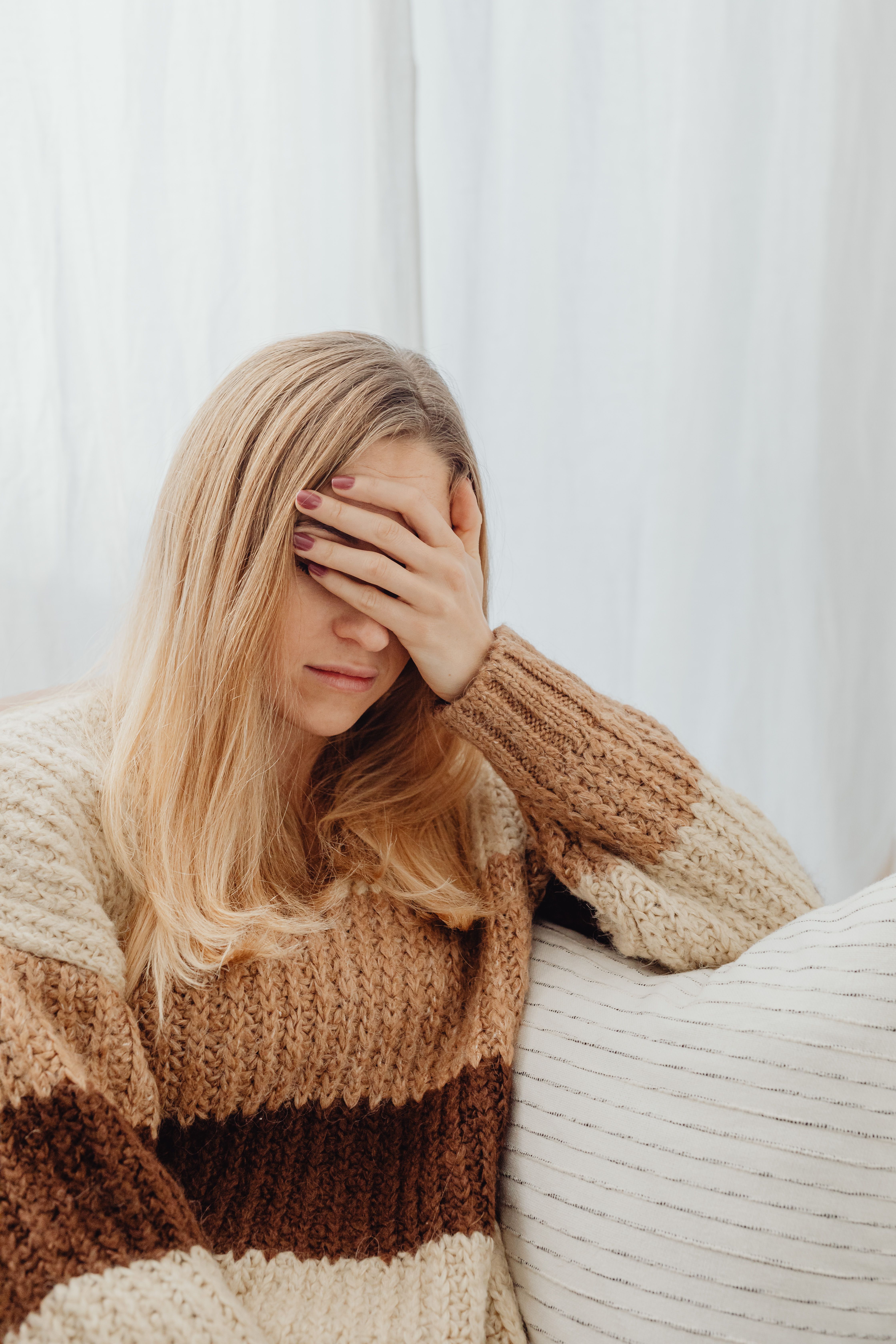 一名女子穿着保暖毛衣，捂着脸坐在室内，显得身体不适