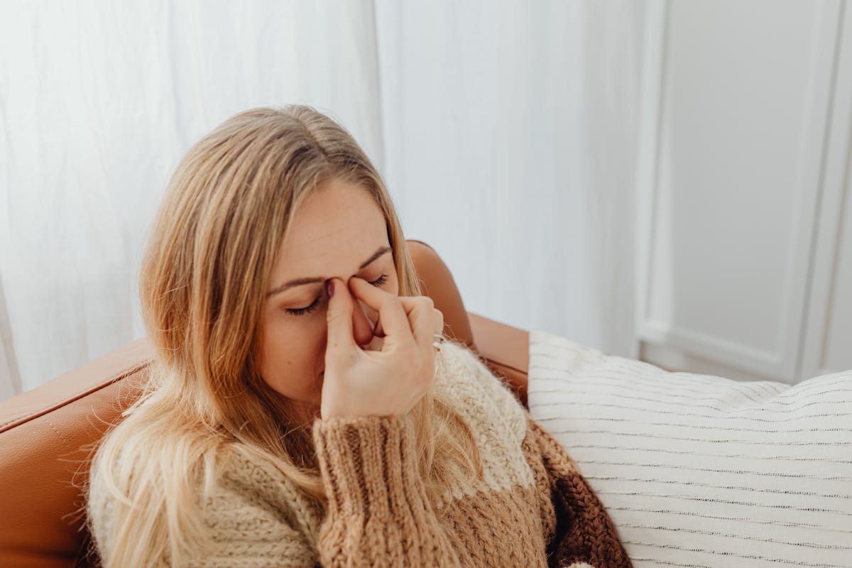 Person sitting on a couch, pinching the bridge of their nose.