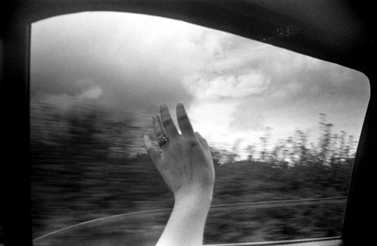 A hand with a ring extends from a car window during an overcast drive.