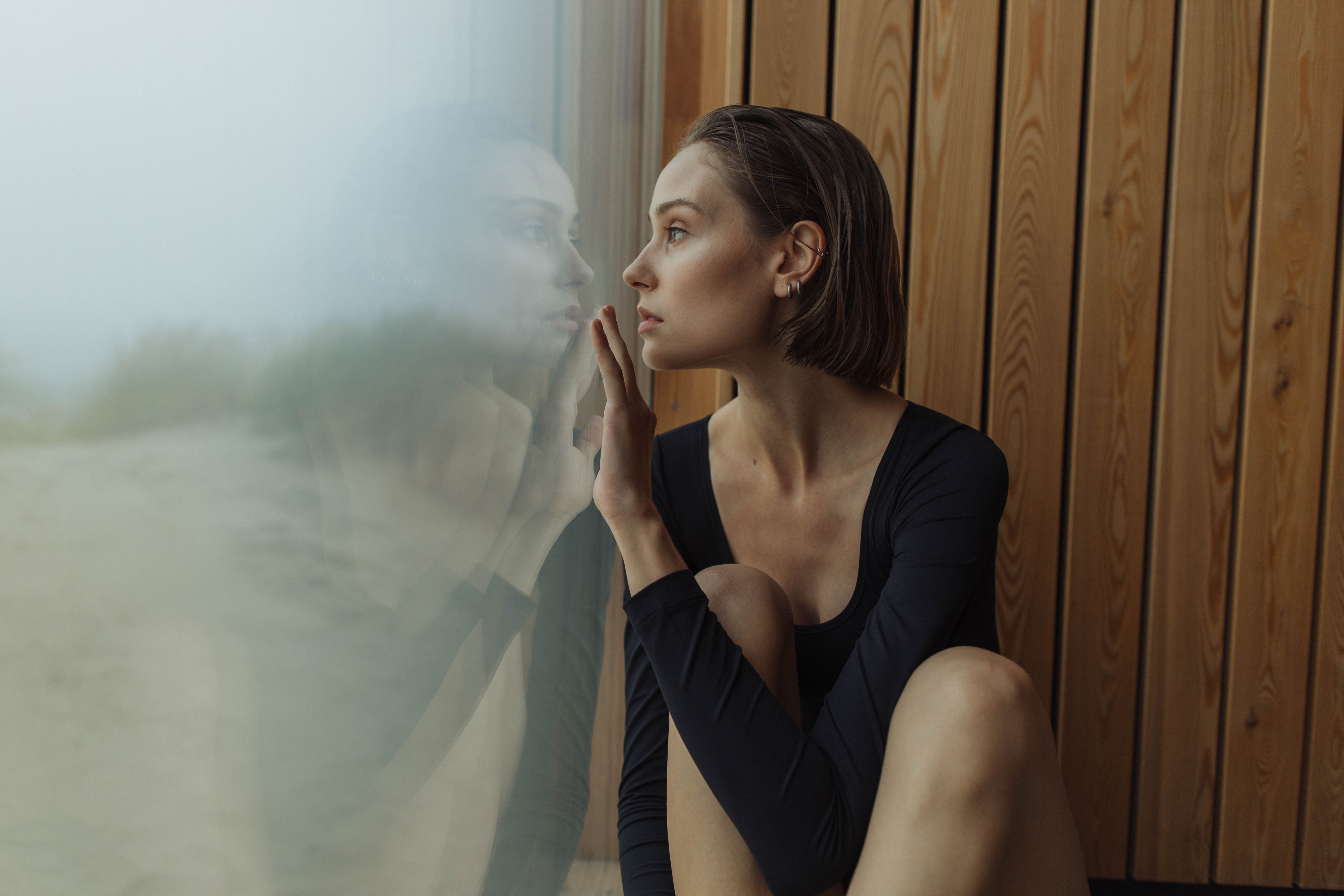 一位女人坐在室内，透过玻璃板凝视，神情深思熟虑，流露出深深的沉思