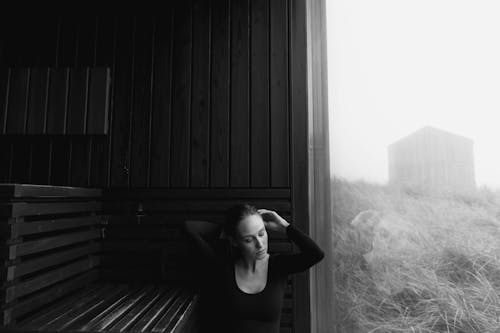 Grayscale Photography of a Woman Sitting Near Wooden Chair