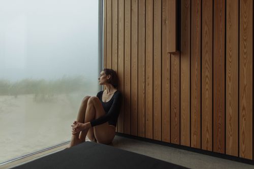 Free Woman in black longsleeve bodysuit sits contemplatively by a foggy window. Stock Photo