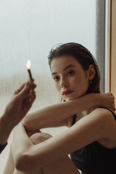 一个女人坐在窗前，手持帕洛桑托手杖，营造出沉思而宁静的氛围
