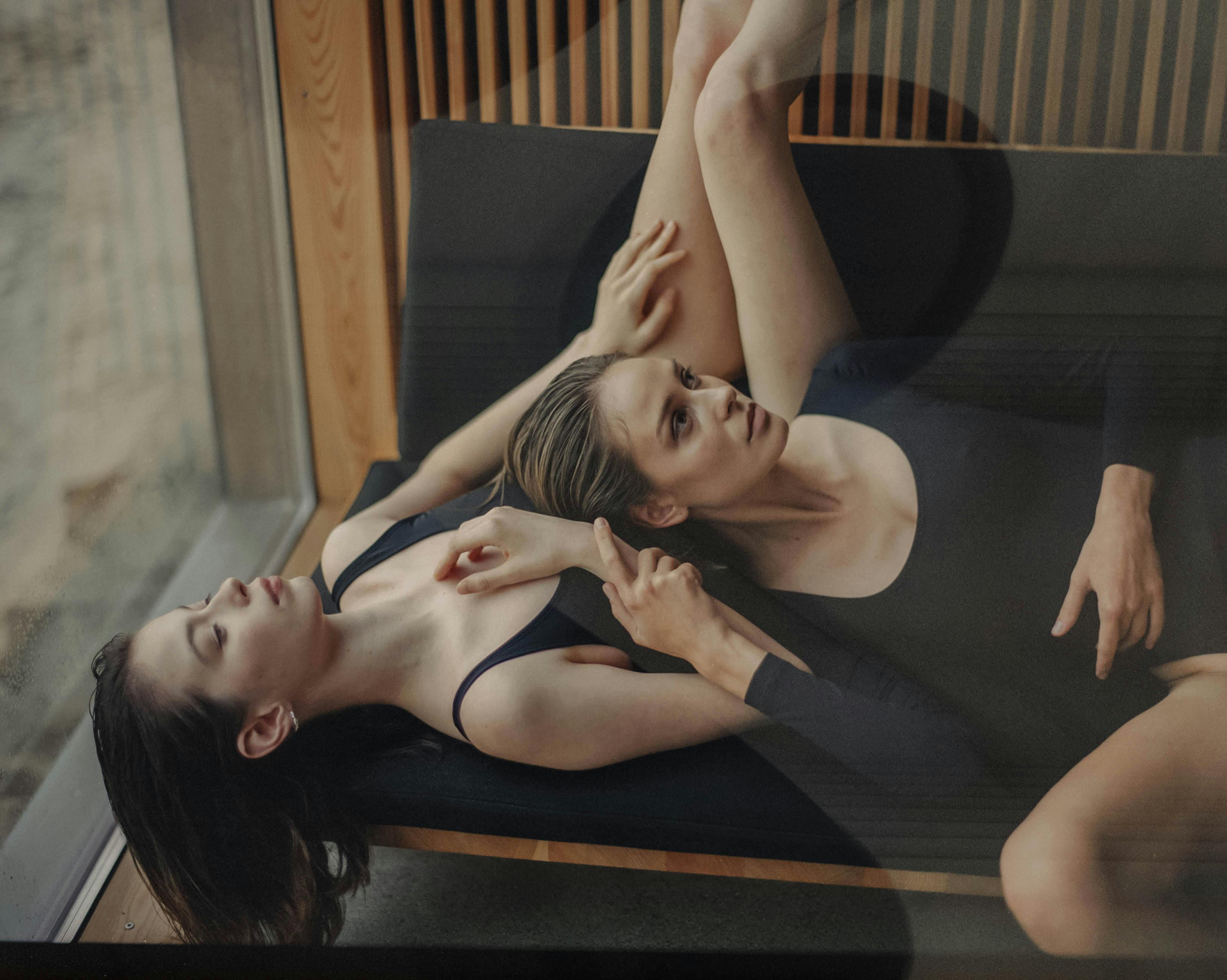 两个穿着黑色衣服的女人在玻璃墙旁的沙发上放松，显得平静而内省