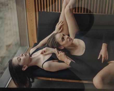 两个穿着黑色衣服的女人在玻璃墙旁的沙发上放松，显得平静而内省