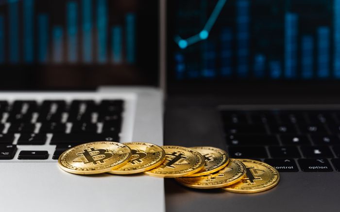 Gold bitcoins placed on laptop keyboards with digital financial graphs in the background.