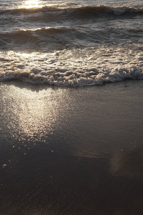 Splashing waves of clean water of sea washing sandy shore in bright sunlight in summer