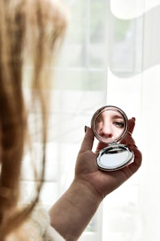 A candid reflection of a woman's face in a handheld mirror, captured indoors.