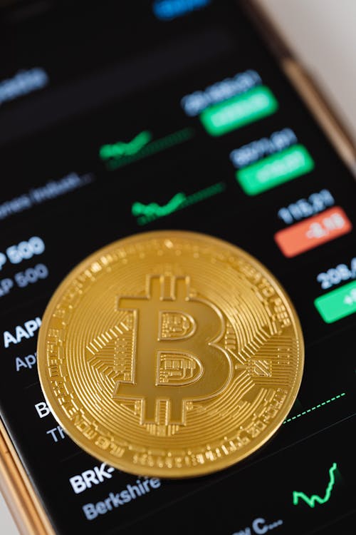 Free Gold Bitcoin Coin Lying on a Phone Displaying Cryptocurrency Graphs  Stock Photo
