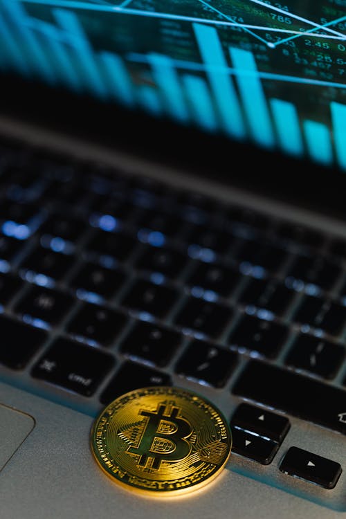 Gold Bitcoin Coin Lying on a Laptop Displaying a Graph 