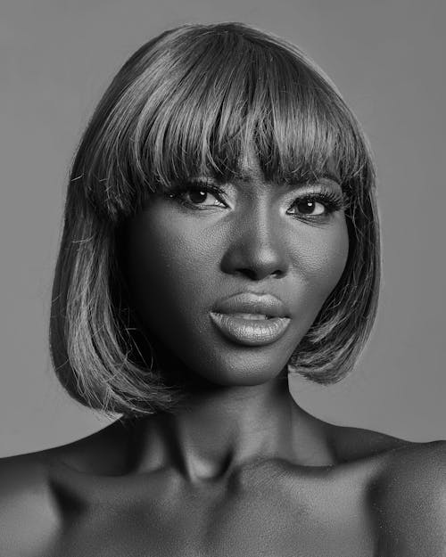 Black and white of African American female with light makeup and bare shoulders standing in studio and looking at camera
