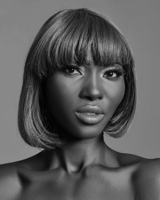 Black and white of African American female with light makeup and bare shoulders standing in studio and looking at camera