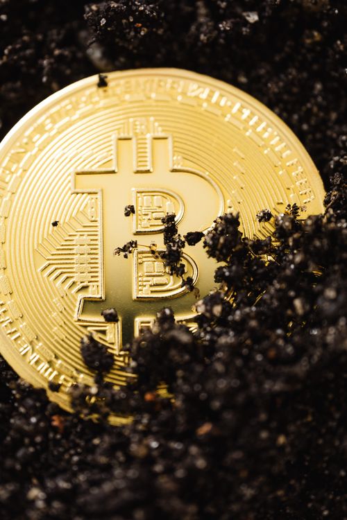Free Close-up of a shiny gold Bitcoin coin partially embedded in dark soil, symbolizing digital currency mining. Stock Photo