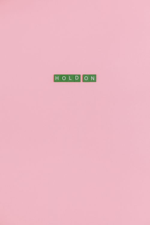 Free Green tiled phrase 'Hold On' on a soft pink background indicating encouragement and perseverance. Stock Photo