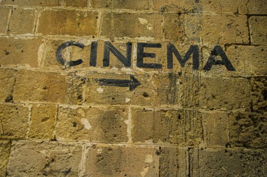 Rustic 'Cinema' sign with arrow spray-painted on old stone wall in Matera, Italy.