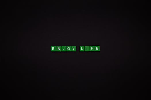 Green letter tiles spelling 'ENJOY LIFE' on a black background, perfect for motivational content.